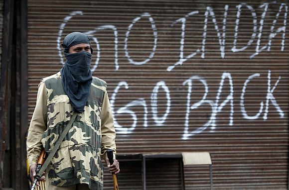 An Indian policeman stands guard near a closed shop during a curfew in Srinagar